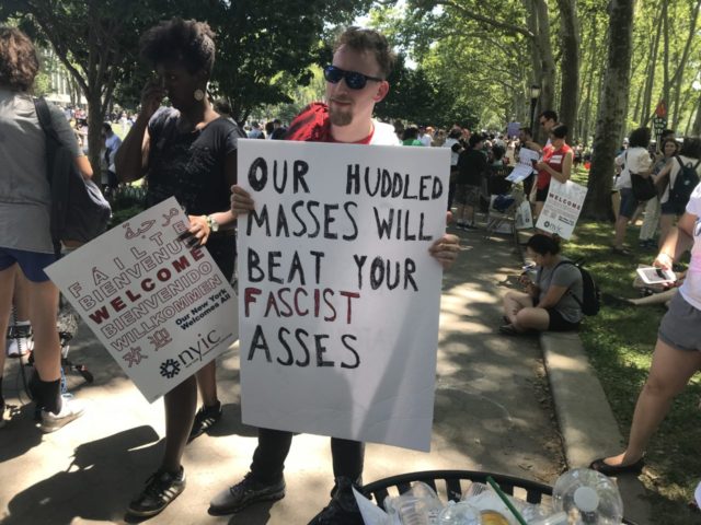 An anti-Trump open borders protester holding a profane sign calling the Trump administrati