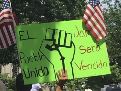 An open borders protester holding a sign depicting a raised fist flanked by two U.S. flags