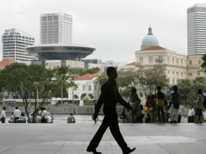 An office worker is silhouetted against the financial district while tourists sit by the waterfront, Friday, Feb. 19, 2010 in Singapore. Singapore raised its 2010 GDP forecast and now expects the city-state's economy to grow as much as 6.5 percent after contracting last year. (AP Photo/Wong Maye-E)