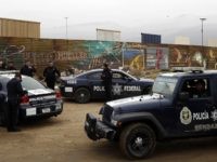 Mexican federal police officers stand guard on the Mexico side of the border on Tuesday, March 13, 2018, in Tijuana, Mexico. President Trump is scheduled to visit the site of the border wall prototypes which can be seen in the background behind the wall. (AP Photo/Gregory Bull)