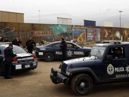 Mexican federal police officers stand guard on the Mexico side of the border on Tuesday, March 13, 2018, in Tijuana, Mexico. President Trump is scheduled to visit the site of the border wall prototypes which can be seen in the background behind the wall. (AP Photo/Gregory Bull)