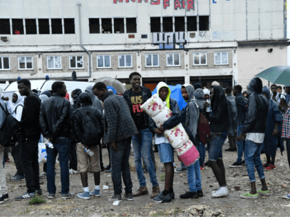 Migrants wait to board buses as police prepare the evacuation of a makeshift camp at Porte