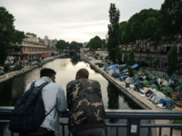 GettyImages-967047310 TOPSHOT - Men look at a makeshift camp during its evacuation by police, along the Canal de Saint-Martin at Quai de Valmy in Paris, on June 4, 2018. - More than 500 migrants and refugees were evacuated on early June 4, 2018 from a makeshift camp that had been set …