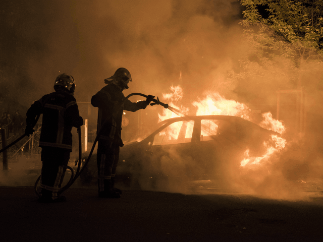 Firefighters work to put out a fire in a car in the Malakoff neighborhood of Nantes early on July 4, 2018. - Groups of young people clashed with police in the western French city of Nantes on the night of July 3 after a man was shot dead by an …