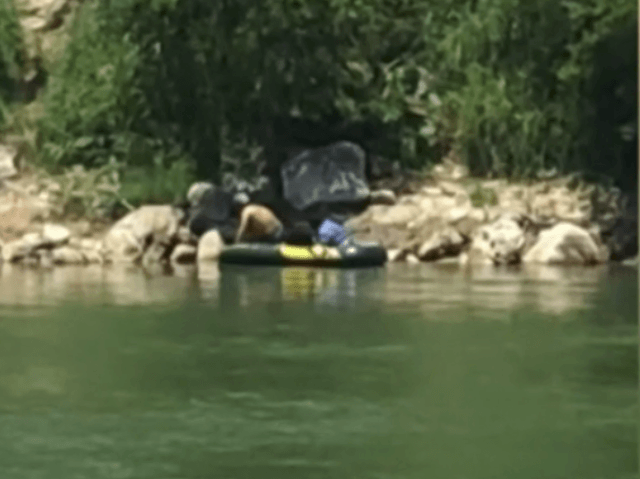 A human smuggler paddles two illegal immigrants across the Rio Grande River in front of a