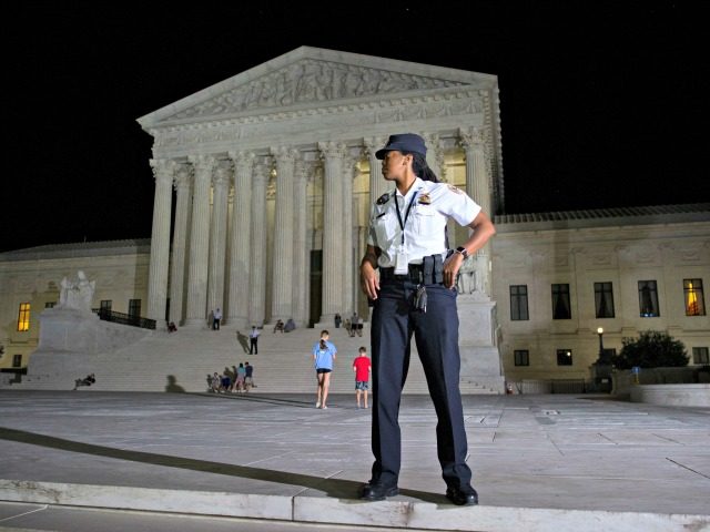 A Supreme Court Police officer stands watch as a protesters demonstrate in front of the Su