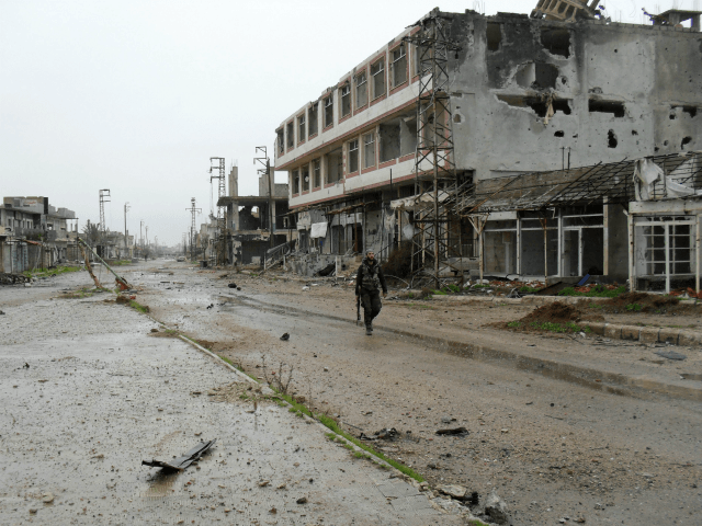 A fighter of Syrian pro-government forces walks past damaged buildings on a street in the