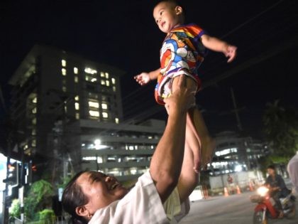 A woman lifts her child near the hospital, seen at left, as ambulance transporting members