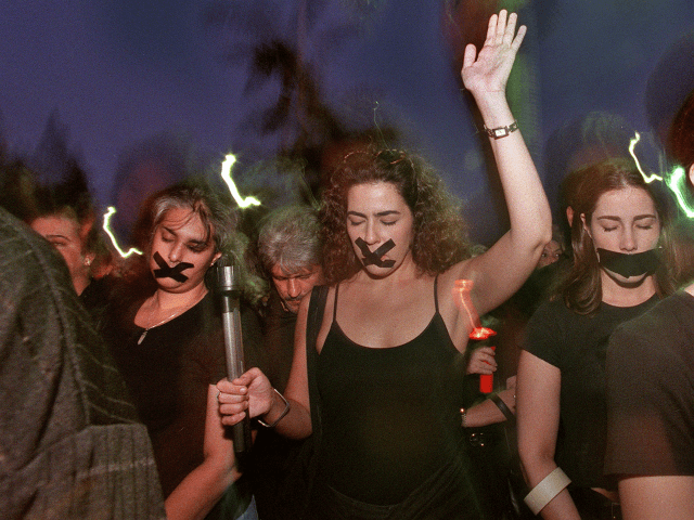 A group of protesters dressed in black with their mouths taped shut march along Miami's be