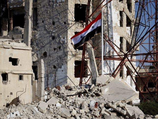 The Syrian national flag rises in the midst of damaged buildings in Daraa-al-Balad, an opp
