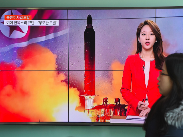 A woman walks past a television screen showing file footage of North Korea's missile launc