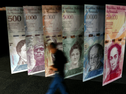 A man walks past banners showing banners depicting Venezuela's currency, the Bolivar, at t
