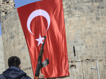 A Turkish policemen holds his AK-47 in front of a huge Turkish flag as he walks in front o