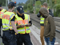 GettyImages-838225820 German policemen check a 16 year-old boy from Eritrea after finding him under a train trailer at the train station in the southern German city of Raubling on August 24, 2017 during a search for illegal migrants on the German-Austrian border. / AFP PHOTO / Guenter SCHIFFMANN (Photo credit should …