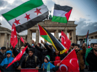 GettyImages-888377708 Demonstrators wave Palestinian, Turkish and Syrian flags in front of the Brandenburg Gate, next to the US embassy in Berlin on December 8, 2017, following US President Donald Trump's decision to recognise Jerusalem as the capital of the Israeli state. / AFP PHOTO / John MACDOUGALL (Photo credit should read …