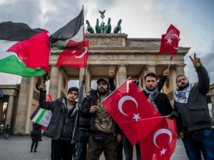 Demonstrators wave Palestinian and Turkish flags in front of the Brandenburg Gate, next to