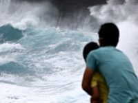 A man from Japan and his son watch as waves crash off sea cliffs along the southeast shore of Oahu as Hurricane Lane approaches, Friday, Aug. 24, 2018 near Honolulu.