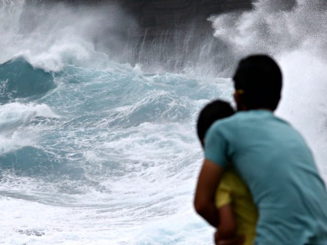 A man from Japan and his son watch as waves crash off sea cliffs along the southeast shore