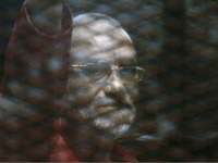 Muslim Brotherhood spiritual leader, Mohammed Badie wearing a red jumpsuit that designates he has been sentenced to death, waves from a defendants cage in a makeshift courtroom at the Torah prison, southern Cairo, Egypt, Tuesday, July 21, 2015. (AP Photo/Amr Nabil)