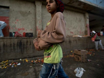 A boy carries two pineapples he found in the trash area of the Coche public market in Caracas, Venezuela. (Fernando Llano/AP)