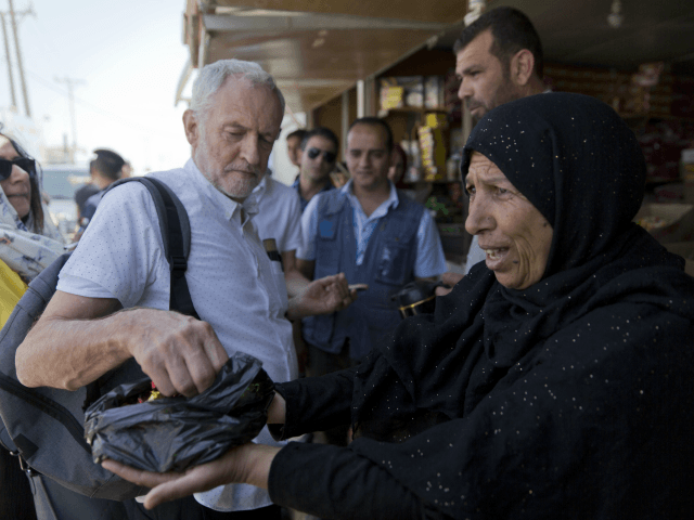 United Kingdom's Labour party leader Jeremy Corbyn is offered candy by Syrian refugee Sohela Sobeihi, 52 while talking to refugees at the main market road, during his visit to the Zaatari Syrian Refugee Camp, in Mafraq, Jordan, Friday, June 22, 2018. (AP Photo/Nasser Nasser)