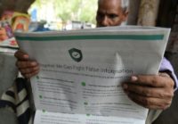 An Indian newspaper vendor reading a newspaper with a full- page advertisement from WhatsApp intended to counter fake information