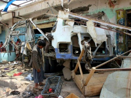 A Yemeni child stands next to the destroyed bus at the site of a Saudi-led coalition air s
