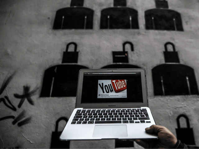 A laptop computer showing Youtube's logo on its screen is held in front of graffiti on Mar