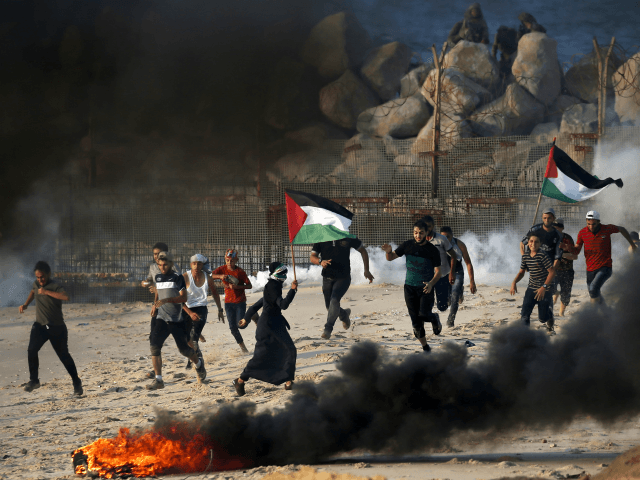Palestinians run from tear gas smoke fired by Israeli forces (background) on the beach near the maritime border with Israel, in the northern Gaza Strip, during a protest calling for the lift of the Israeli blockade on the coastal Palestinian enclave, on September 10, 2018. (Photo by SAID KHATIB / …