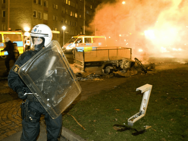 A riot police officer stands guard while colleagues extinguish burning barricades on the main road in the heavily-immigrant populated neighborhood of Rosengaard of the southern Swedish city of Malmoe on December 19, 2008. Some 100 youths rioted in late December 18 for the second straight night, setting cars and garbage …
