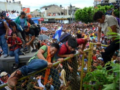 Thousands of Honduran migrants gather at a fence as some climb towards Mexico in Tecun Uman, Guatemala, Friday, Oct. 19, 2018. Migrants broke down the gates at the border crossing and began streaming toward a bridge into Mexico. After arriving at the tall, yellow metal fence some clambered atop it …