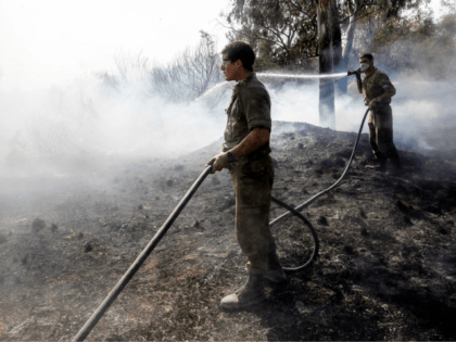 Israeli soldiers attempt to extinguish a fire in a forest field near the Kibbutz of Nahal Oz, along the border with the Gaza Strip, on July 17 after it was caused by inflammable material attached to a balloon flown by Palestinian protesters from across the border. (Photo by MENAHEM KAHANA …