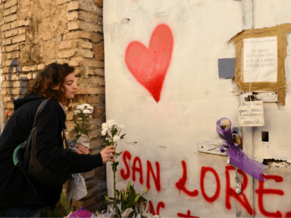 A young woman places flowers at the entrance of a sequestered derelict building in the San Lorenzo district of Rome on October 24, 2018, a week after a female teenager was found dead in the building. - The body of sixteen-year-old Desiree Mariottini was found dead overnight on October 19 …