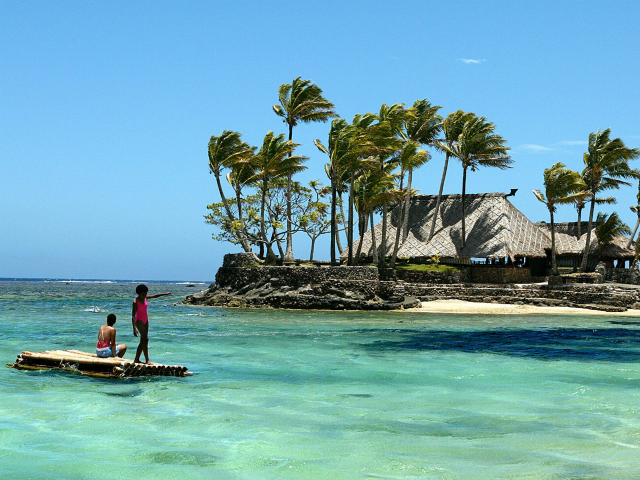 Melanesian children float on a bamboo pontoon by Wicked Walu Island on the resort-studded