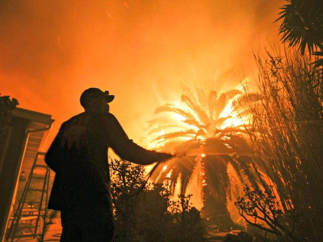 Park Billow, 27, sprays water on the hot spots in his backyard as the Woolsey Fire burns i