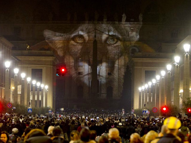 People gather to watch images projected on the facade of St. Peter's Basilica, at the Vati