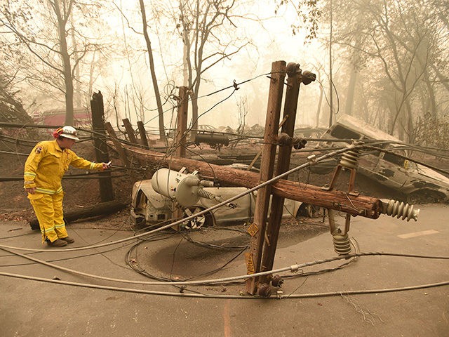 TOPSHOT - CalFire firefighter Scott Wit surveys burnt out vehicles near a fallen power line on the side of the road after the Camp fire tore through the area in Paradise, California on November 10, 2018. - Firefighters in California on November 10 battled raging blazes at both ends of …