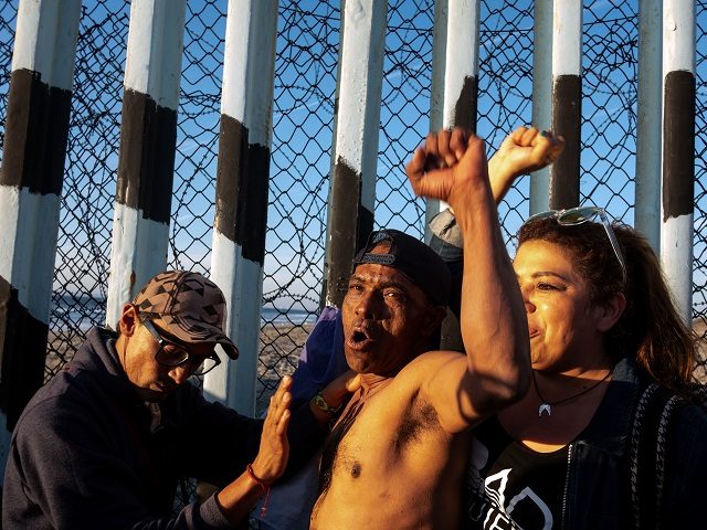 A Honduran migrant (C), cheers for Mexico as locals support him at the US-Mexico border wa