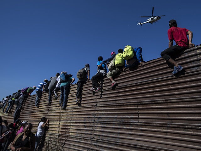 TOPSHOT - A group of Central American migrants -mostly Hondurans- climb a metal barrier on