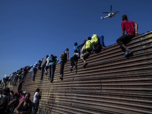 A group of Central American migrants -mostly Hondurans- climb a metal barrier on the Mexic