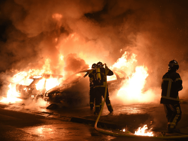 TOPSHOT - Firefighters work to put out a fire as cars burn in the Le Breil neighborhood of Nantes early on July 7, 2018. - A French policeman who shot dead a young black man in western France earlier this week, sparking four nights of rioting, has been charged with …