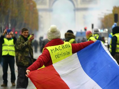 A woman wears a Yellow vest (Gilet jaune) reading 'Macron resign' on the Champs Elysees in Paris, on November 24, 2018 during a protest against rising oil prices and living costs. - Police fired tear gas and water cannon on November 24 in central Paris against 'yellow vest' protesters demanding …