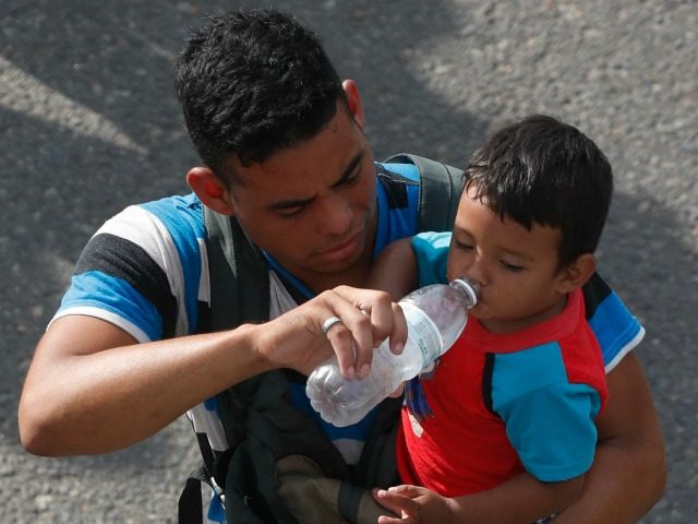 A man carrying a boy gives the child water while walking with a caravan of Central America