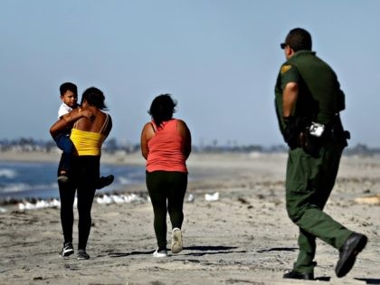 Two women, one carrying a child, walk north after crossing illegally into the United States as a Border Patrol agent moves in to detain them Wednesday, Nov. 14, 2018, seen from Tijuana, Mexico. Migrants in a caravan of Central Americans scrambled to reach the U.S. border, catching rides on buses …