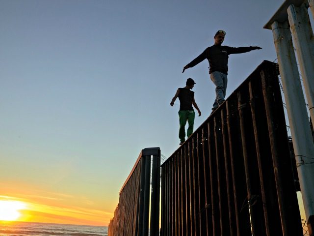 Two Central American migrants walk along the top of the border structure separating Mexico