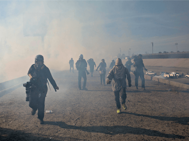 Migrants run from tear gas launched by U.S. agents, amid photojournalists covering the Mex