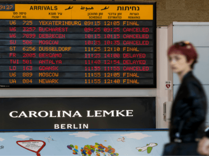 A passenger walks past an information board indicating delayed or cancelled flights during