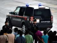 Italian police stand guard as migrants and refugees, mainly from Nigeria, Ghana, Senegal and Sierra Leone who were transported by the German navy frigate Werra as part of the European external action service EU Navfor Med, arrive at the Augusta harbour in eastern Italy on September 27, 2015. Some 500 …