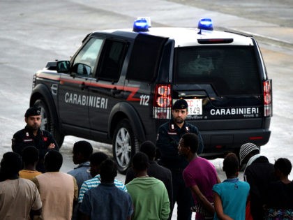 Italian police stand guard as migrants and refugees, mainly from Nigeria, Ghana, Senegal and Sierra Leone who were transported by the German navy frigate Werra as part of the European external action service EU Navfor Med, arrive at the Augusta harbour in eastern Italy on September 27, 2015. Some 500 …