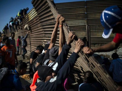 TOPSHOT - A group of Central American migrants -mostly Hondurans- climb the border fence between Mexico and the United States as others try to bring it down, near El Chaparral border crossing, in Tijuana, Baja California State, Mexico, on November 25, 2018. - Hundreds of migrants attempted to storm a …